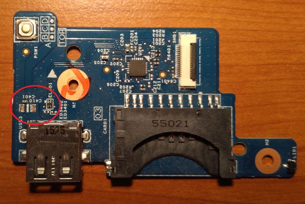 Vyjmutá IO daughterboard z notebooku s USB-A konektorem a SD card slotem; viditelné stopy oranžového tavného lepidla u upevňovacího otvoru