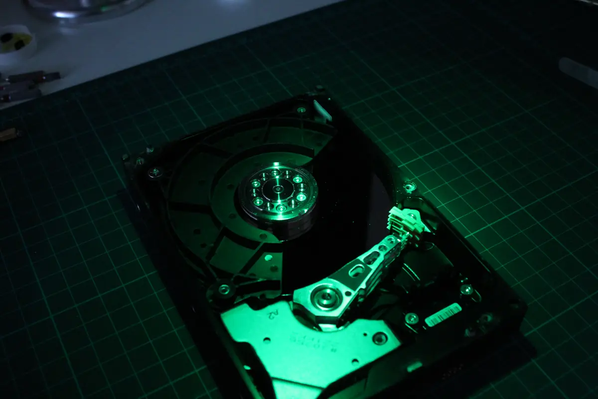 Otevřený 3,5 palcový pevný disk na zelené řezací podložce, nasvícený zeleným studiovým světlem — viditelný spindle, plotna a parkovací rameno hlav