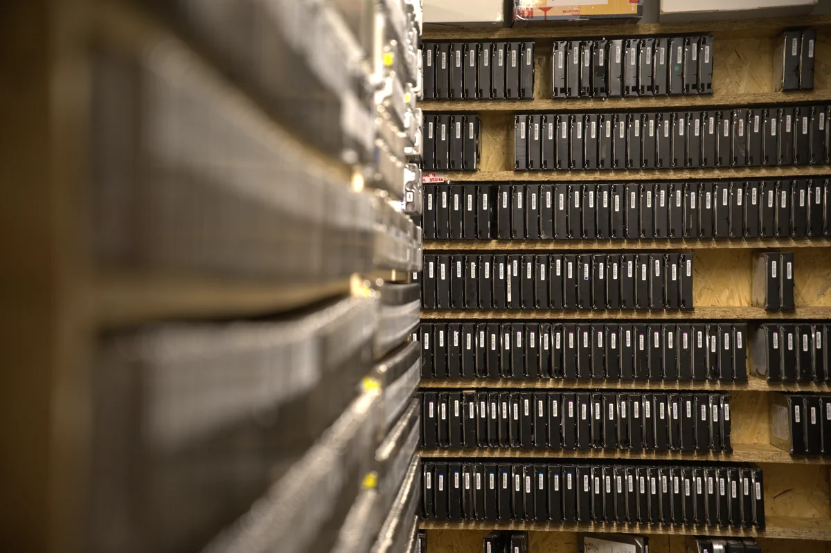 Regály s archivem pevných disků v laboratoři ITHOPE Brno — desítky modelů 3,5 palcových HDD seřazené v dílenských pozicích