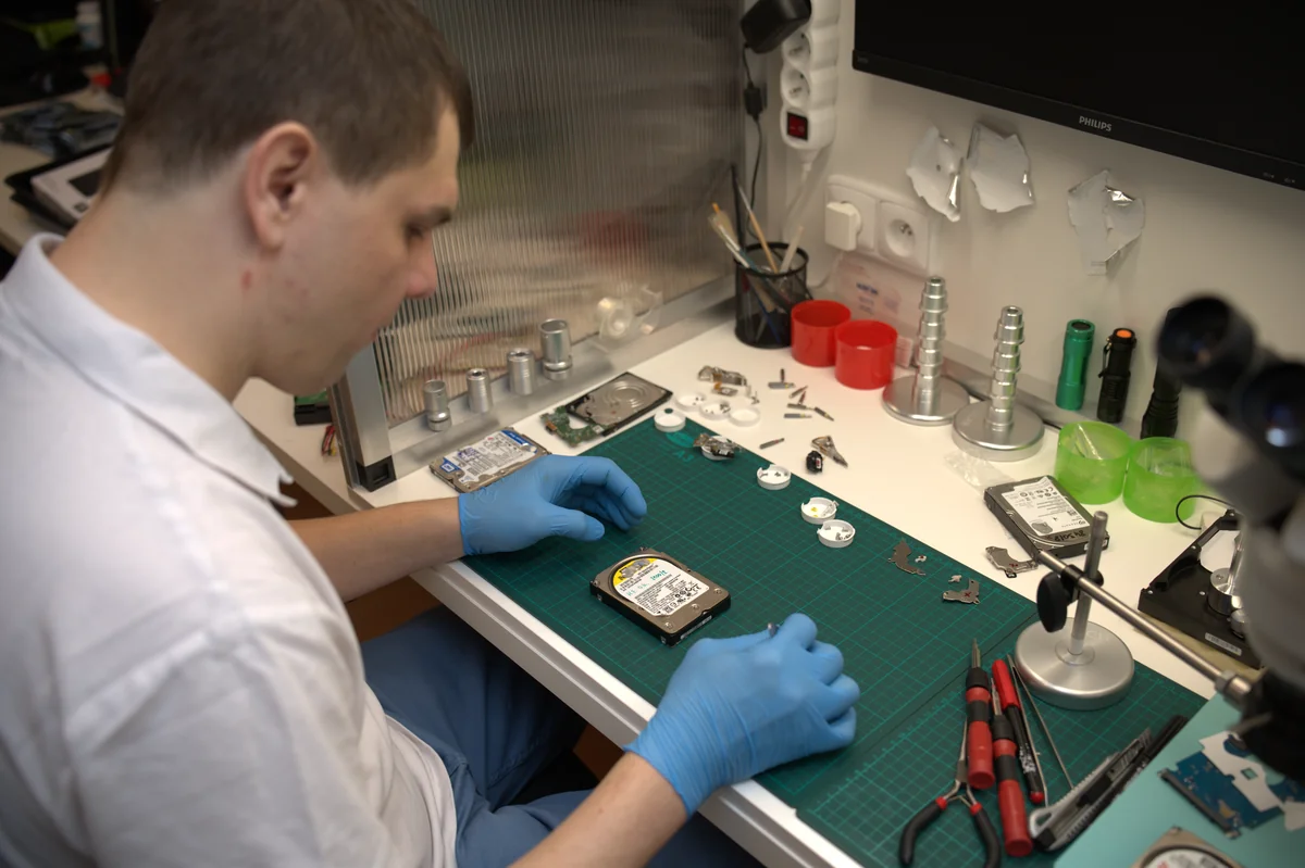 Технік у нітрилових рукавичках працює з відкритим 3,5-дюймовим HDD на зеленому антистатичному килимку, поряд стереомікроскоп і набір прецизійних викруток