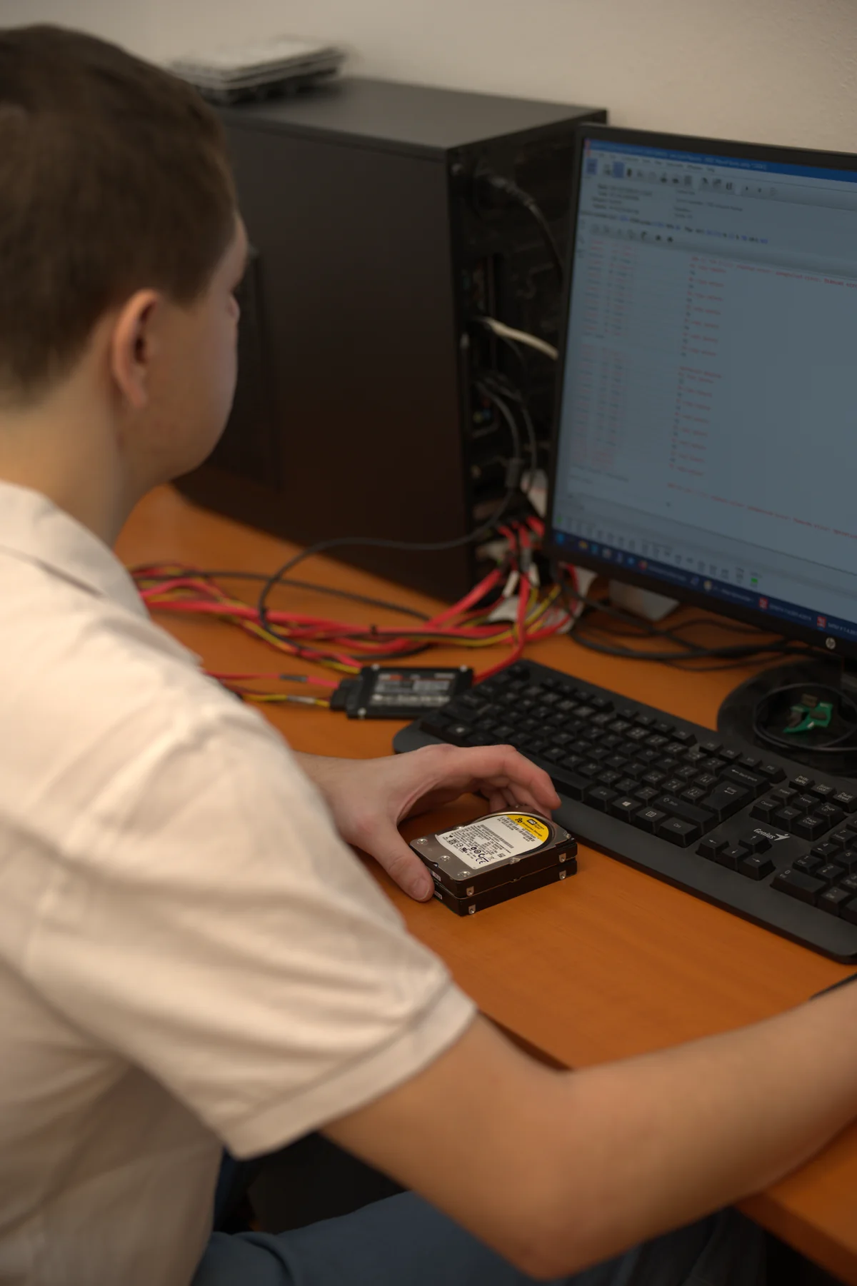 A technician in the Brno workshop holds two 2.5" Western Digital disks; on the desk a 2.5" Samsung SSD connected via a USB-SATA bridge, with file-extraction recovery software on the monitor
