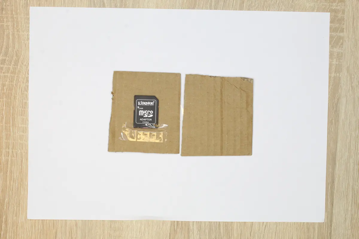 Eine Anleitung zum sicheren Versand einer Speicherkarte per Post — eine microSD-Karte in einem Adapter, eingeklebt zwischen zwei Stücken Wellpappe